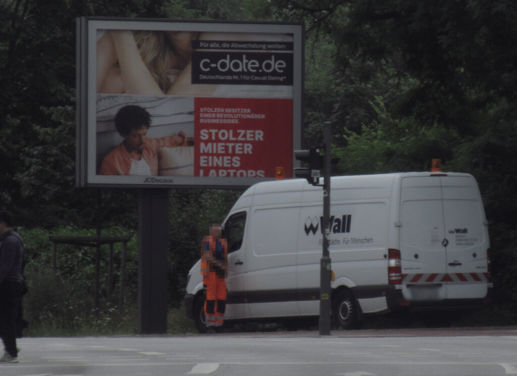 Eine Werbeglotze von Decaux mit "c-date.de" und "Stolzer Mieter eines Laptops" mit Servicefahrzeug (Transporter) und Angestelltem davor.